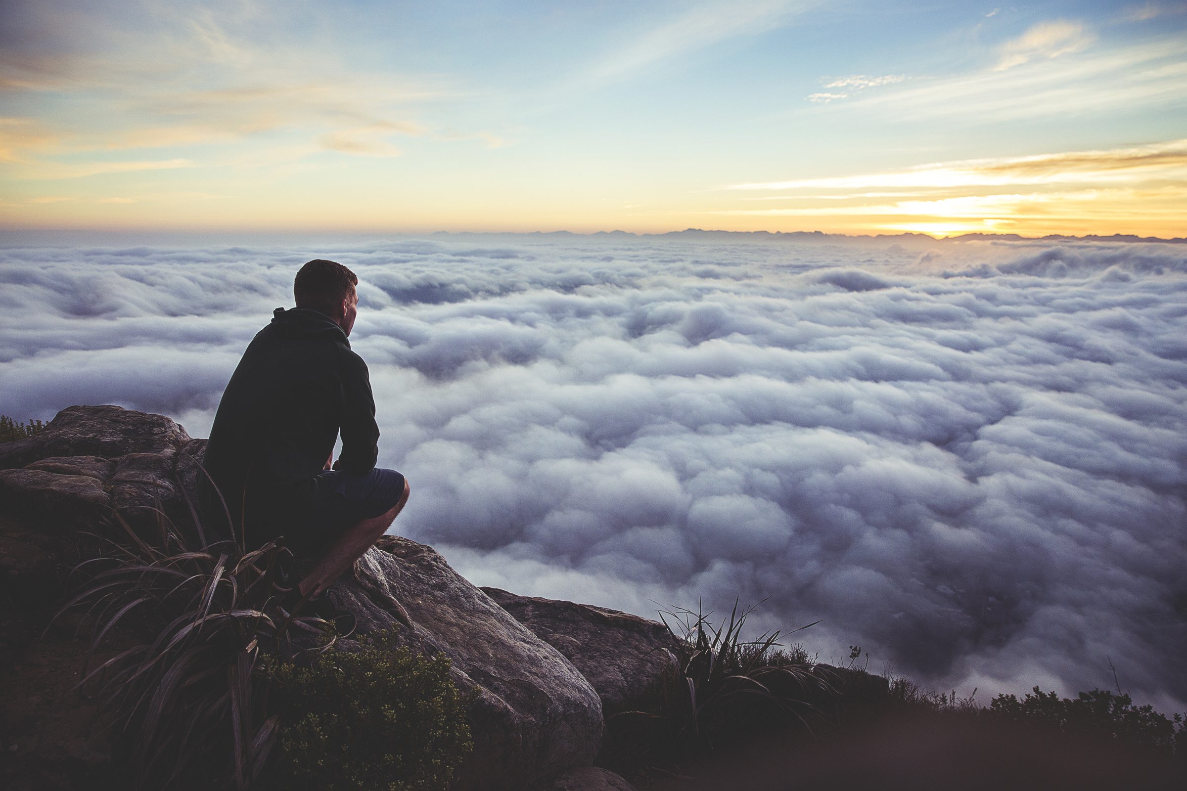 A man sitting on a mountain top above a sea of clouds